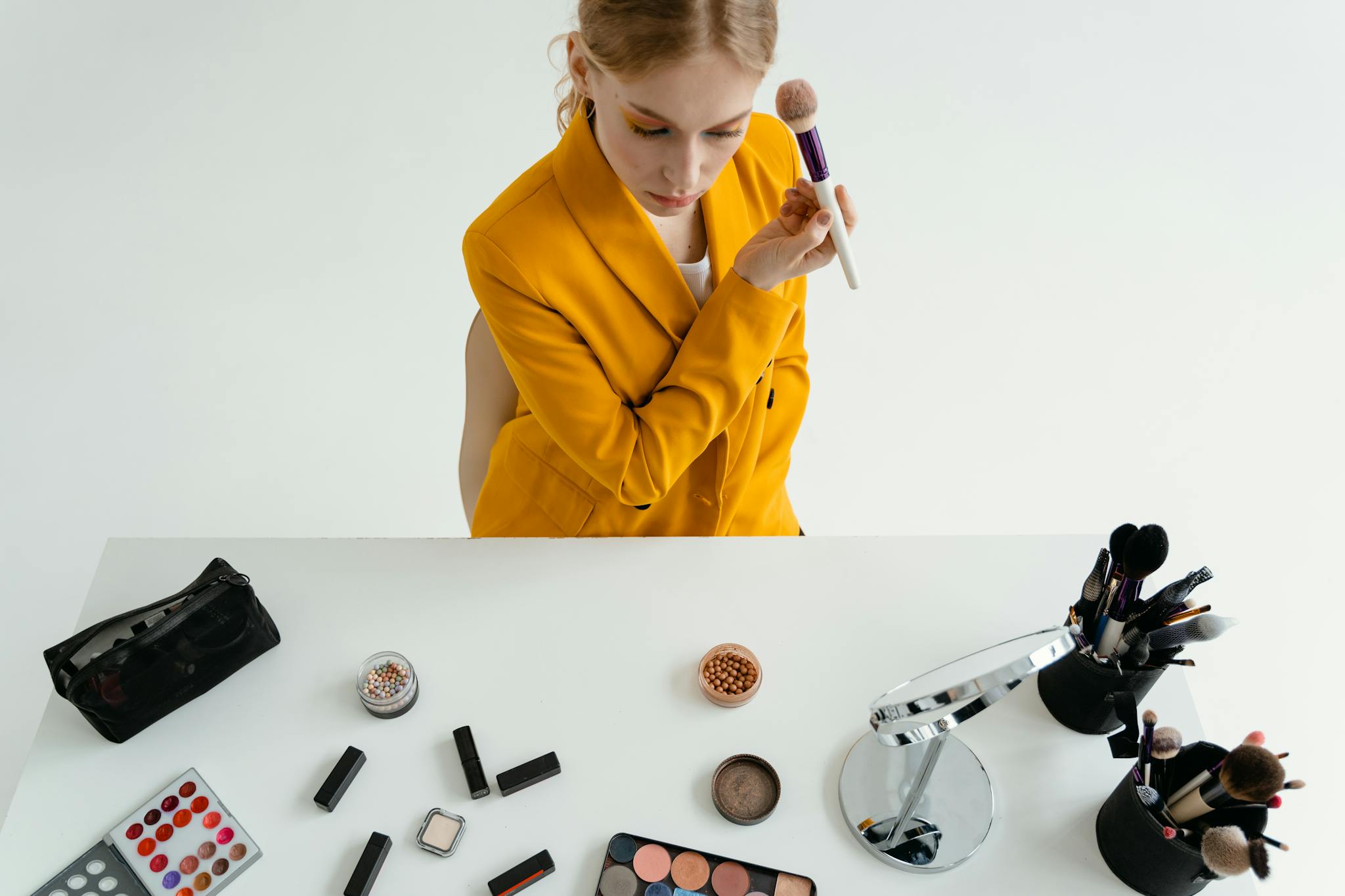 A woman in a yellow blazer applying makeup at a stylish vanity setup.